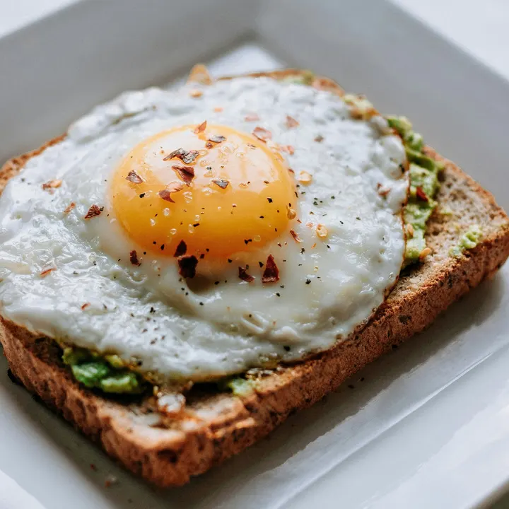Smashed avocado on toast topped with a fried egg and chilli flakes