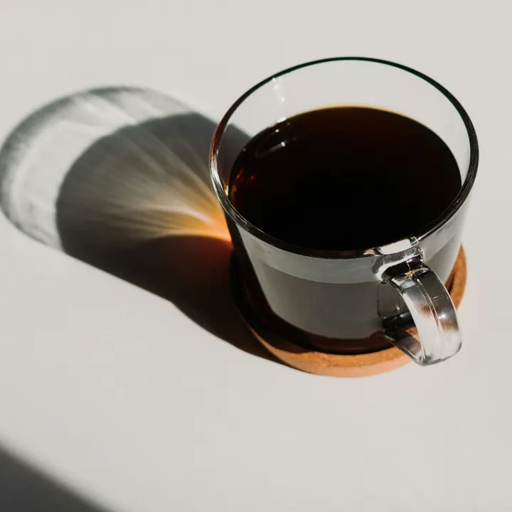 A long black in a glass cup on a cork coaster in bright sunlight